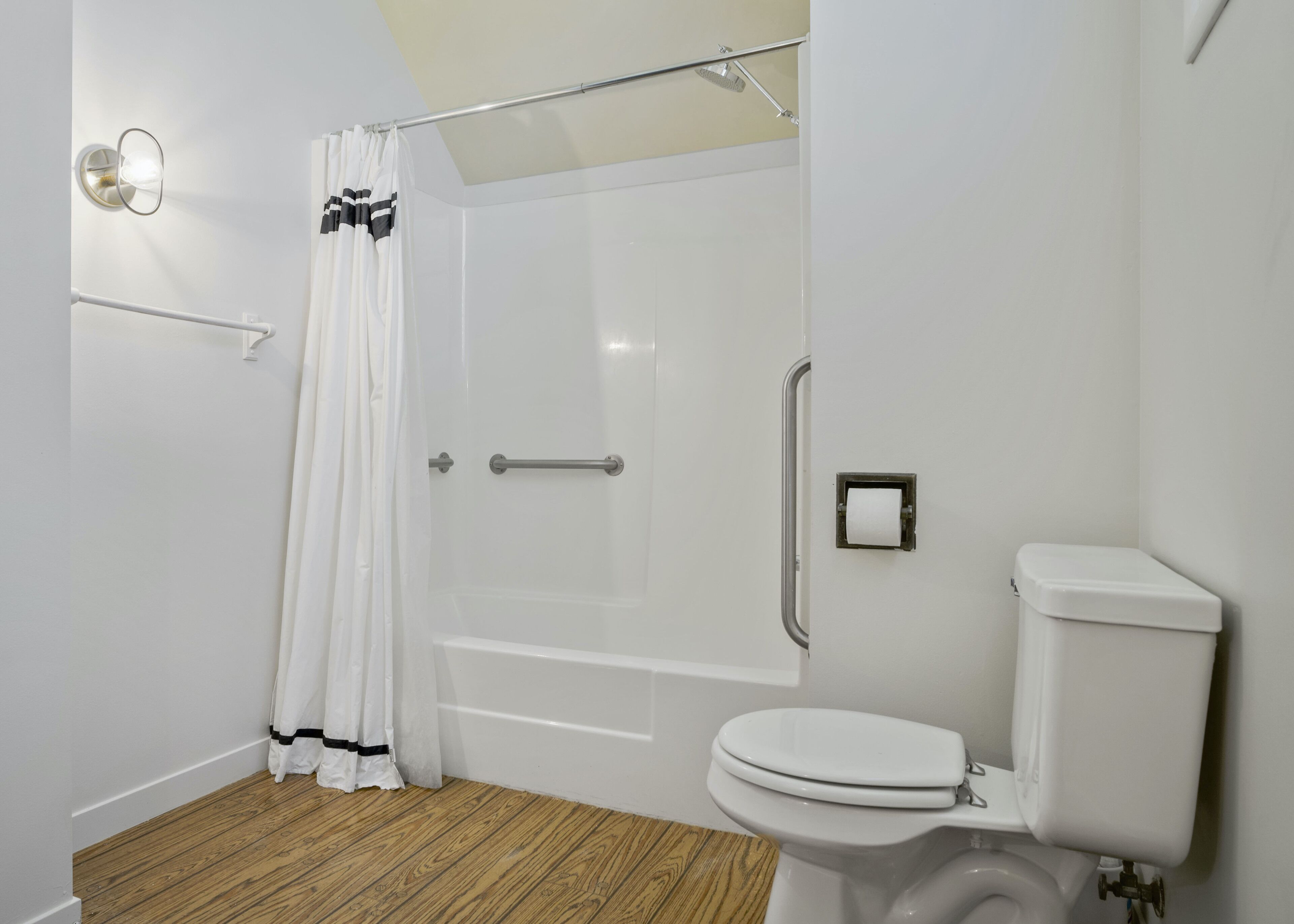 A modern bathroom with a shower, toilet, and a handrail.