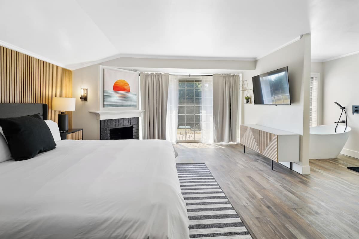 Quarto de hotel moderno com uma cama grande, lareira, televisão e varanda com cortinas.