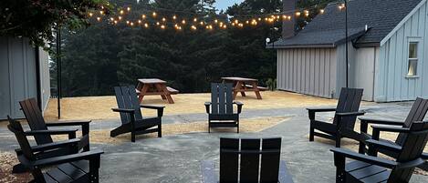 A patio area with Adirondack chairs, a picnic table, and string lights.