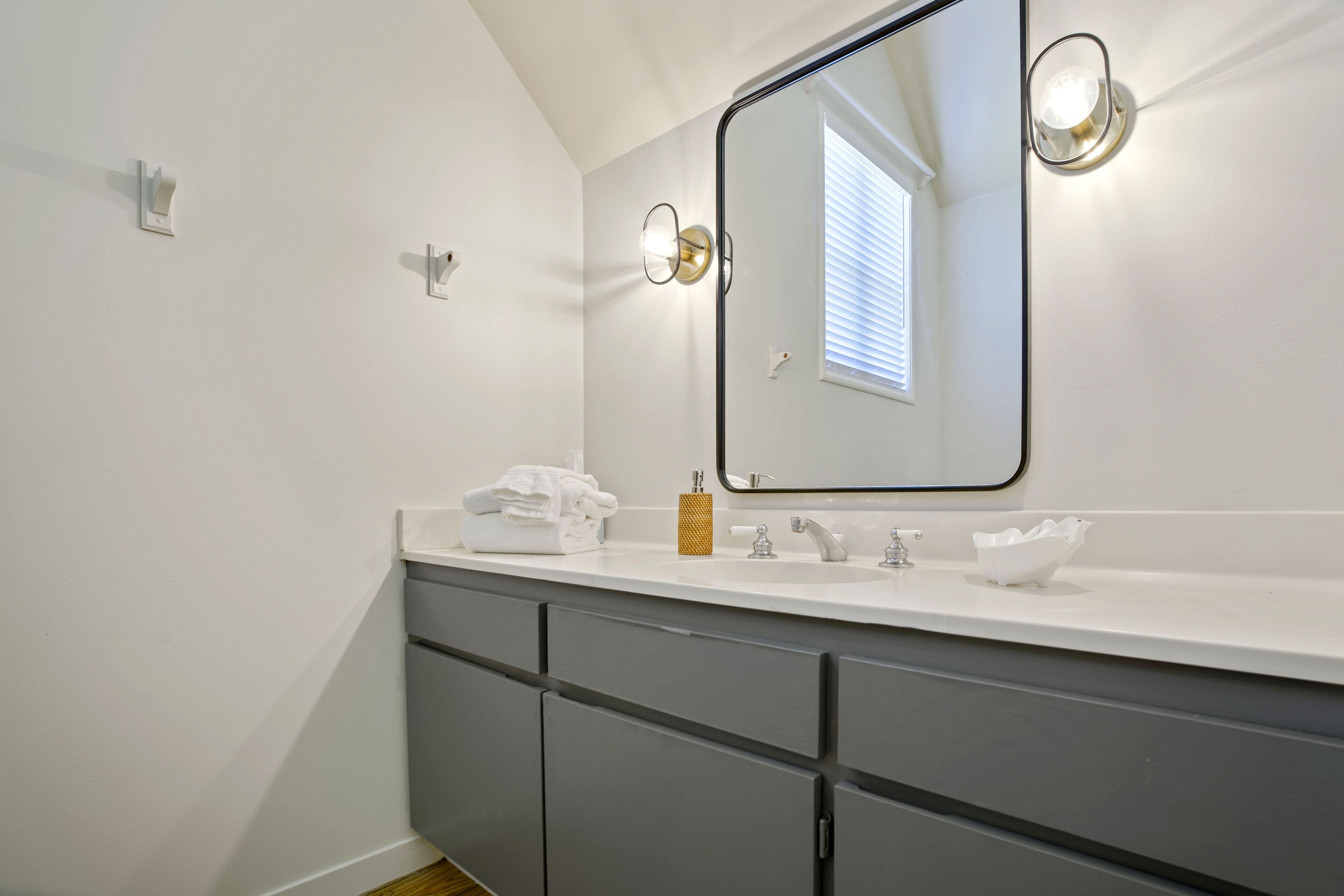 A modern bathroom with a large mirror, white vanity, and grey cabinets.