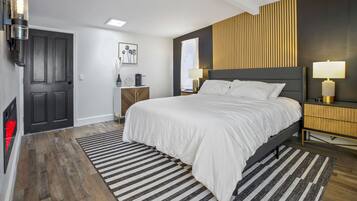 A modern bedroom with a large bed, a wooden headboard, a nightstand with a lamp, and a striped rug.