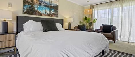 Una habitación de hotel con una cama grande, una mesita de noche, una lámpara, una silla y un ventanal con cortinas.