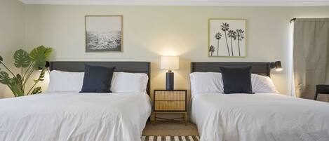 A hotel room with two beds, a nightstand, a lamp, and two framed pictures on the wall.