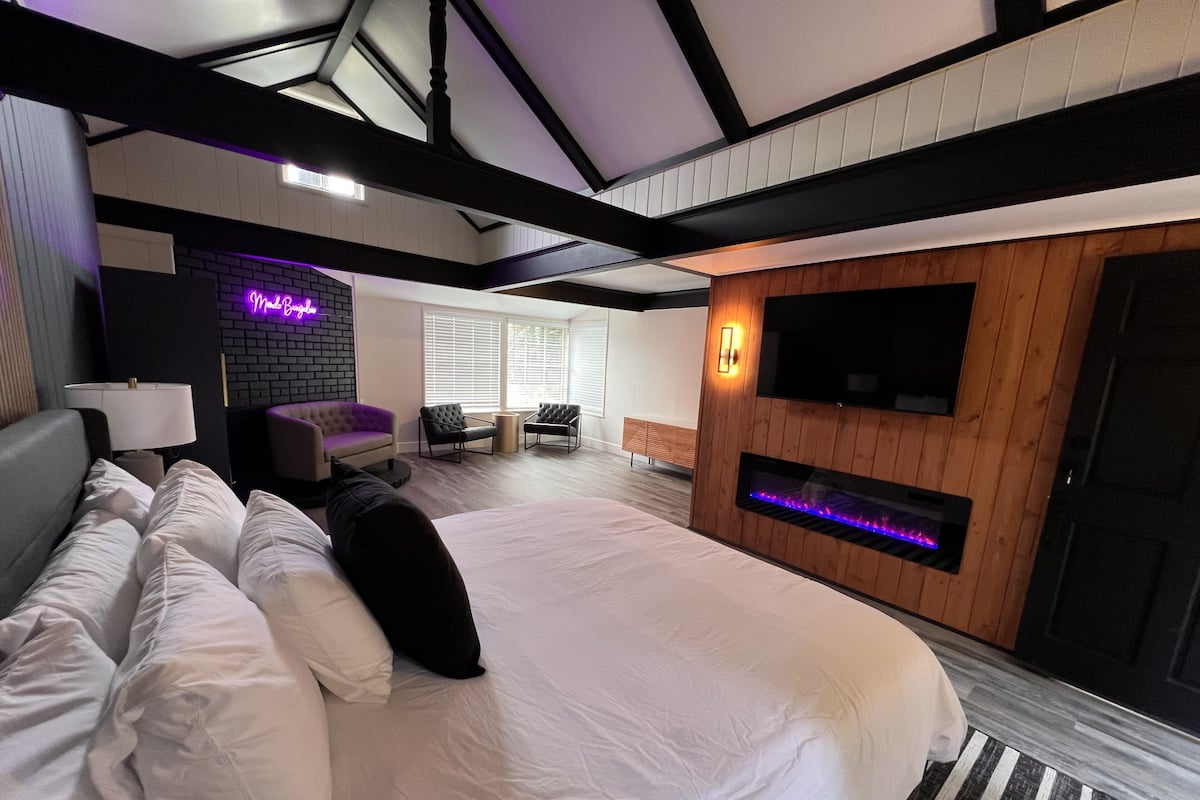 Quarto de hotel moderno com uma cama grande, televisão de tela plana, lareira e um letreiro de neon.