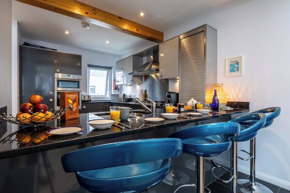 A modern kitchen with a central island, bar stools, and a breakfast setup.