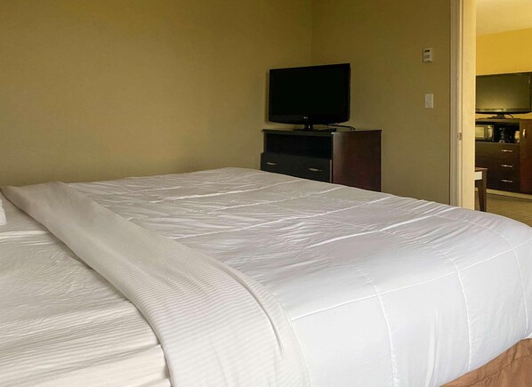 Een hotelkamer met een groot bed, een flatscreen televisie op een standaard en een houten dressoir.
