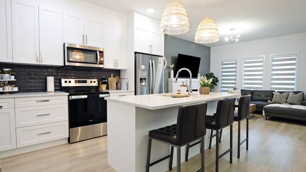 A modern kitchen with white cabinets, stainless steel appliances, and a central island with bar stools. - BoHo Modern Retreat w/King|Fireplace|Disney+ (Edmonton)