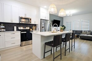 Une cuisine moderne avec des meubles blancs, des appareils en acier inoxydable et un îlot central doté de tabourets de bar.