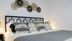 Una cama bien tendida con una colcha estampada y varias almohadas, un cabecero geométrico y decoración artística en la pared.