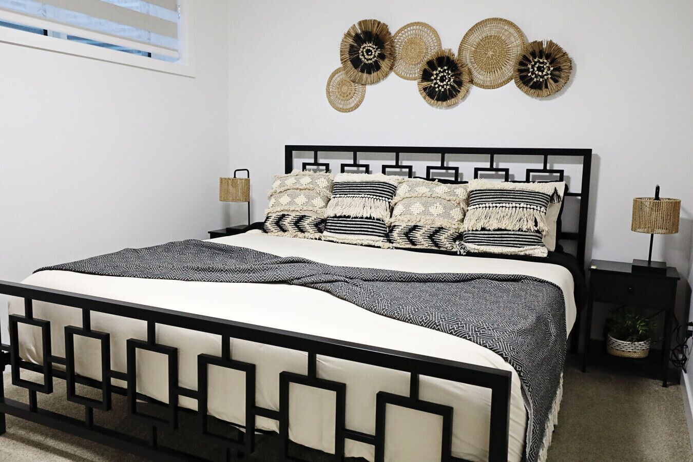 A modern bedroom with a black metal bed frame, a white and black patterned bedspread, and decorative wall art above the bed.