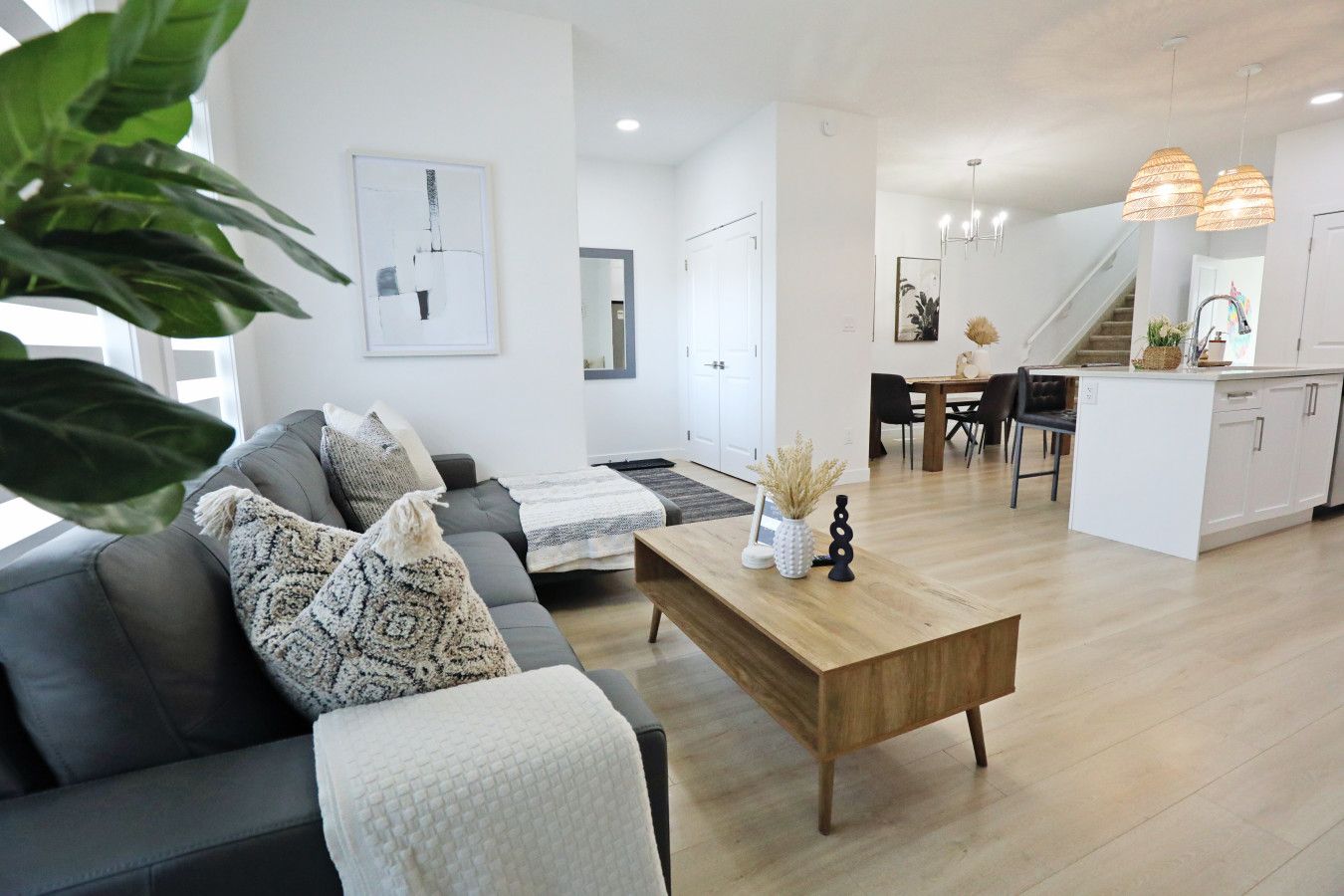 Un salon moderne avec un canapé gris, une table basse en bois et un coin repas comprenant un îlot blanc et des chaises noires.