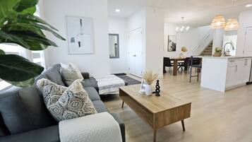 Un salon moderne avec un canapé gris, une table basse en bois et un coin repas comprenant un îlot blanc et des chaises noires.