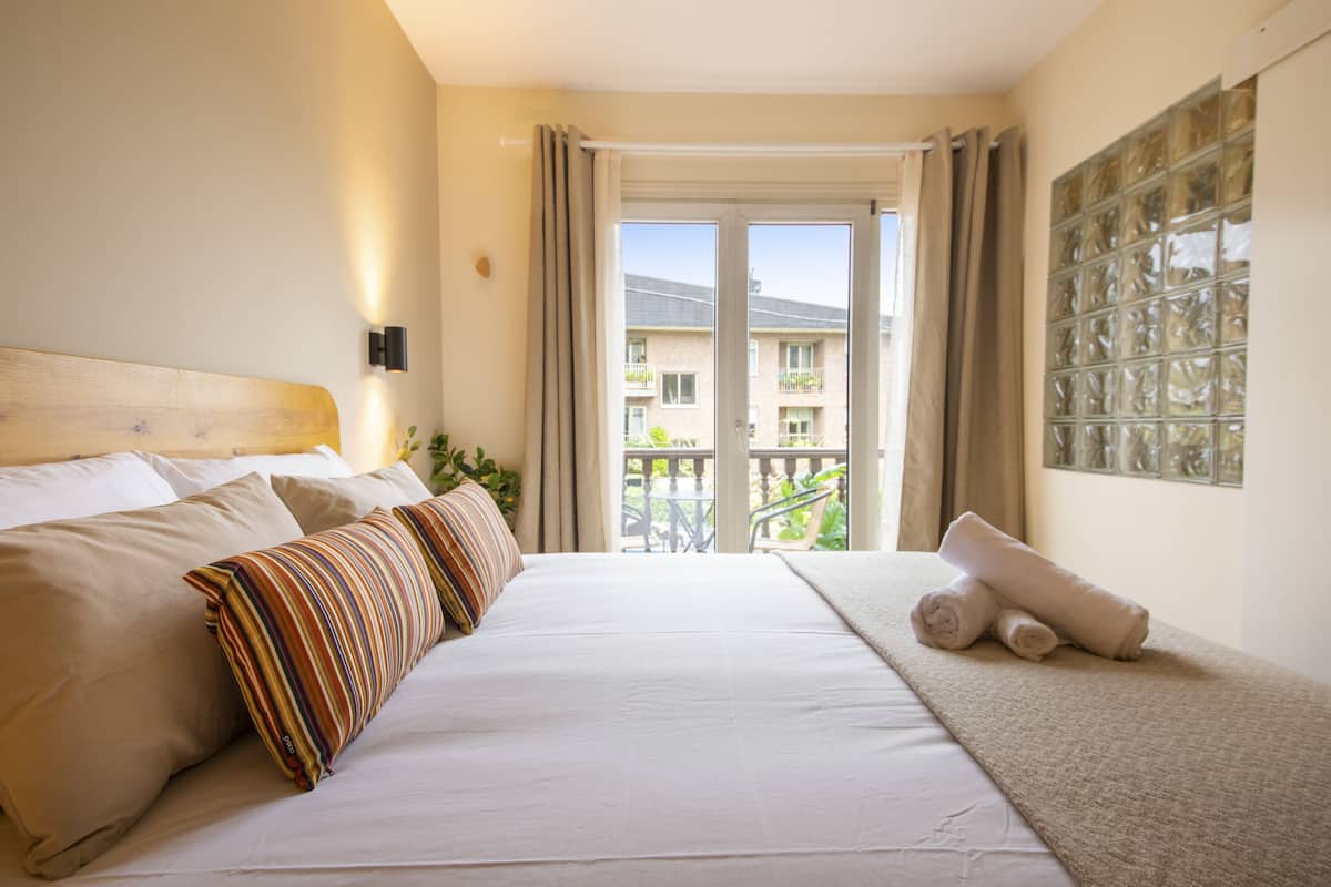 A hotel room with a large bed, a view of the balcony, and a window with a decorative glass panel.