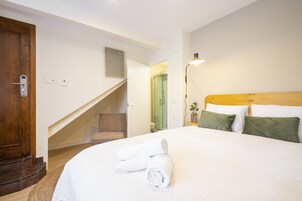 A hotel room with a bed, a wooden headboard, a nightstand, a lamp, a chair, and a staircase leading to another room.
