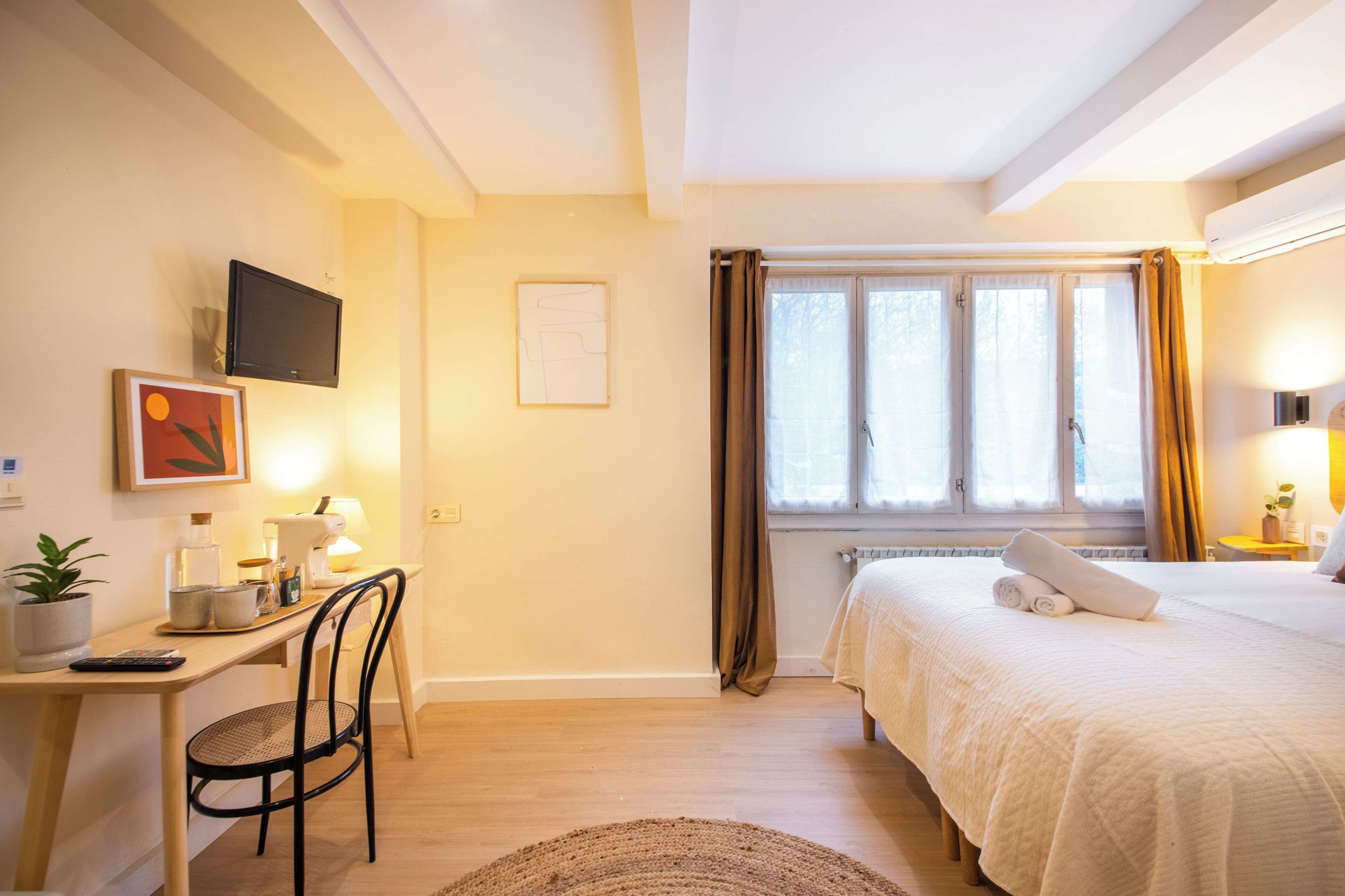 Een hotelkamer met een bed, een bureau met stoel, een televisie en een raam met gordijnen.