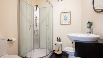 A bathroom with a glass-enclosed shower, a toilet, a sink, and a framed botanical print on the wall.