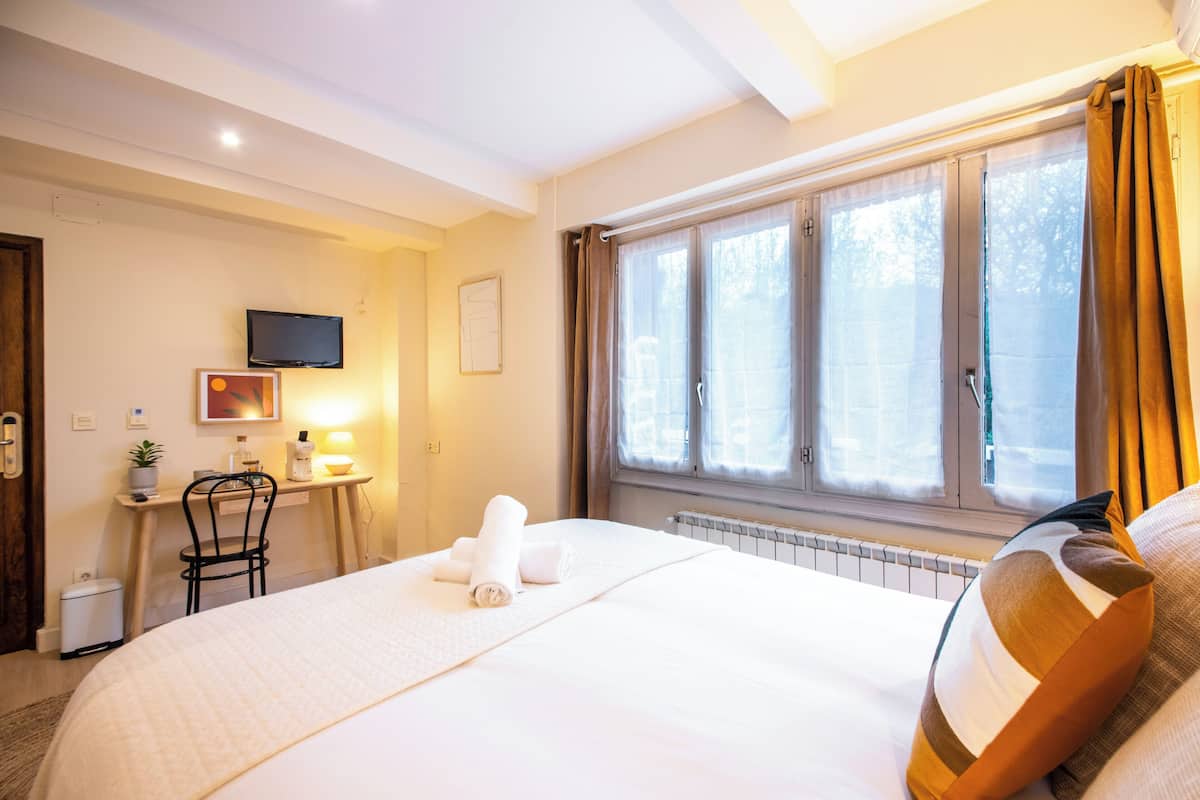 A hotel room with a bed, a desk with a chair, a television, and a window with curtains.