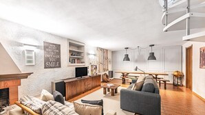 En moderne stue med pejs, sofa, spisebord og et køkkenområde med indbygget reol.