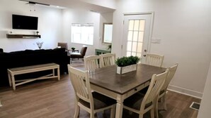 A dining area with a wooden table and white chairs, a bench, and a TV mounted on the wall. - Spacious, Updated 4-bedroom Home near Short North Arts / Entertainment District (Columbus)