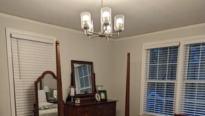 A bedroom with a four-poster bed, a wooden dresser, a mirror, and a chandelier. - Master's Tournament Rental (Augusta)