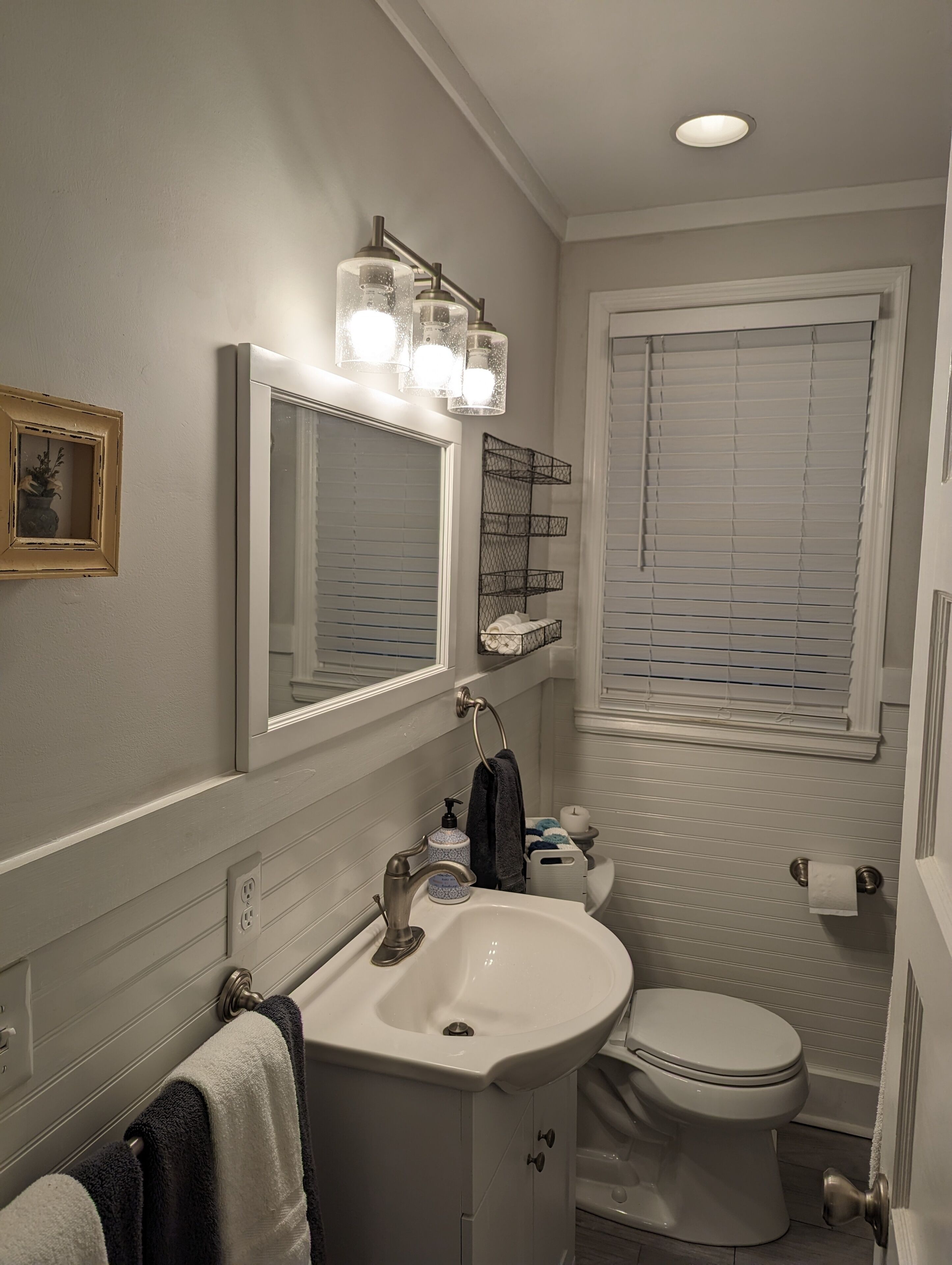A bathroom with a white sink, a mirror, a toilet, and a window with blinds.