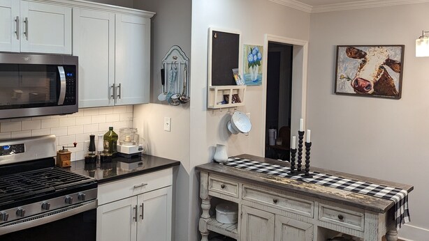 A modern kitchen with white cabinetry, stainless steel appliances, and a wooden island with a checkered tablecloth. - Charming Country Cottage Near Augusta National (Augusta)
