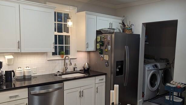 Una cocina moderna con armarios blancos, un refrigerador de acero inoxidable, una lavadora integrada y un mantel a cuadros.