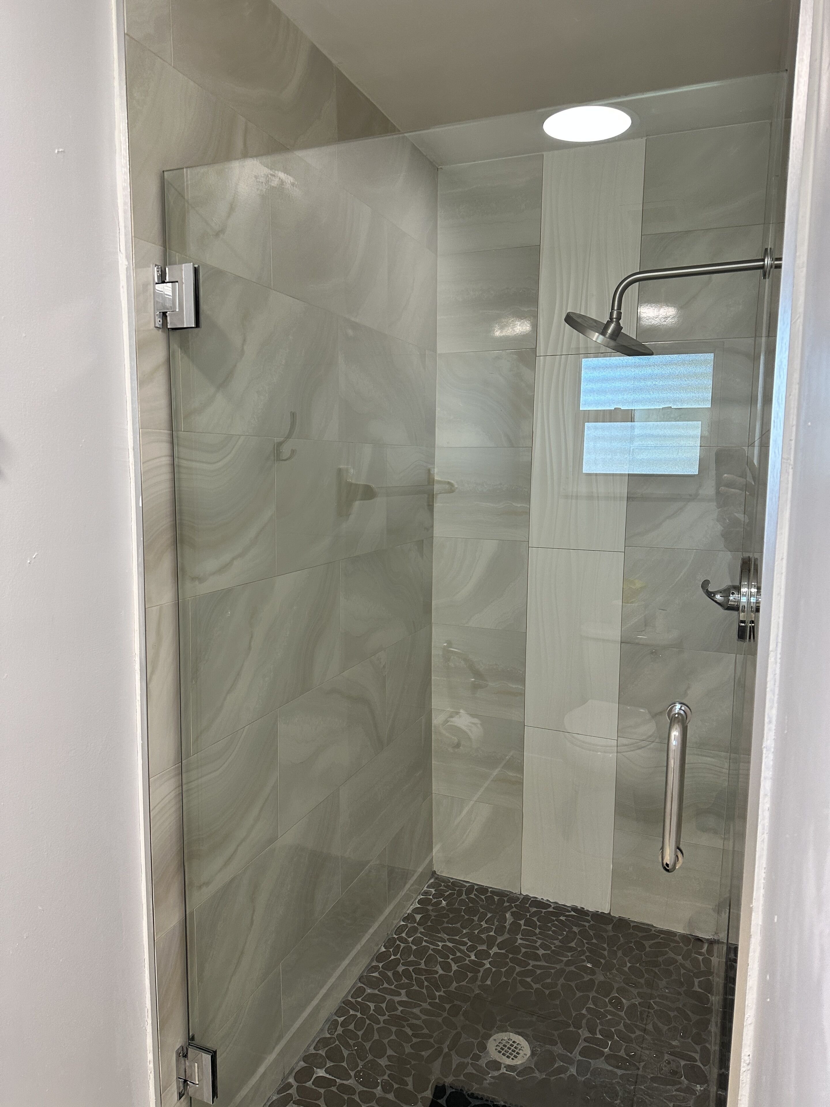Una ducha a nivel con puerta de cristal, cabezal de ducha de mano y control de ducha de mano.