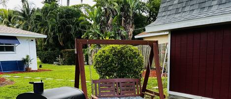 A backyard with a barbecue grill, a swing set, and a shed.