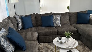 A modern living room with a sectional sofa, two coffee tables, and a large window.