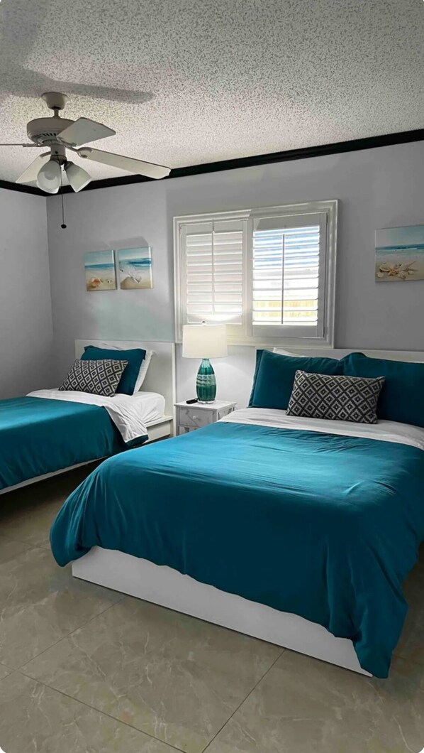 A bedroom with two beds, a ceiling fan, a window with blinds, and artwork on the walls. - Casa Lakehouse 3BD 3BH Heated Pool Lake View (Fort Myers)