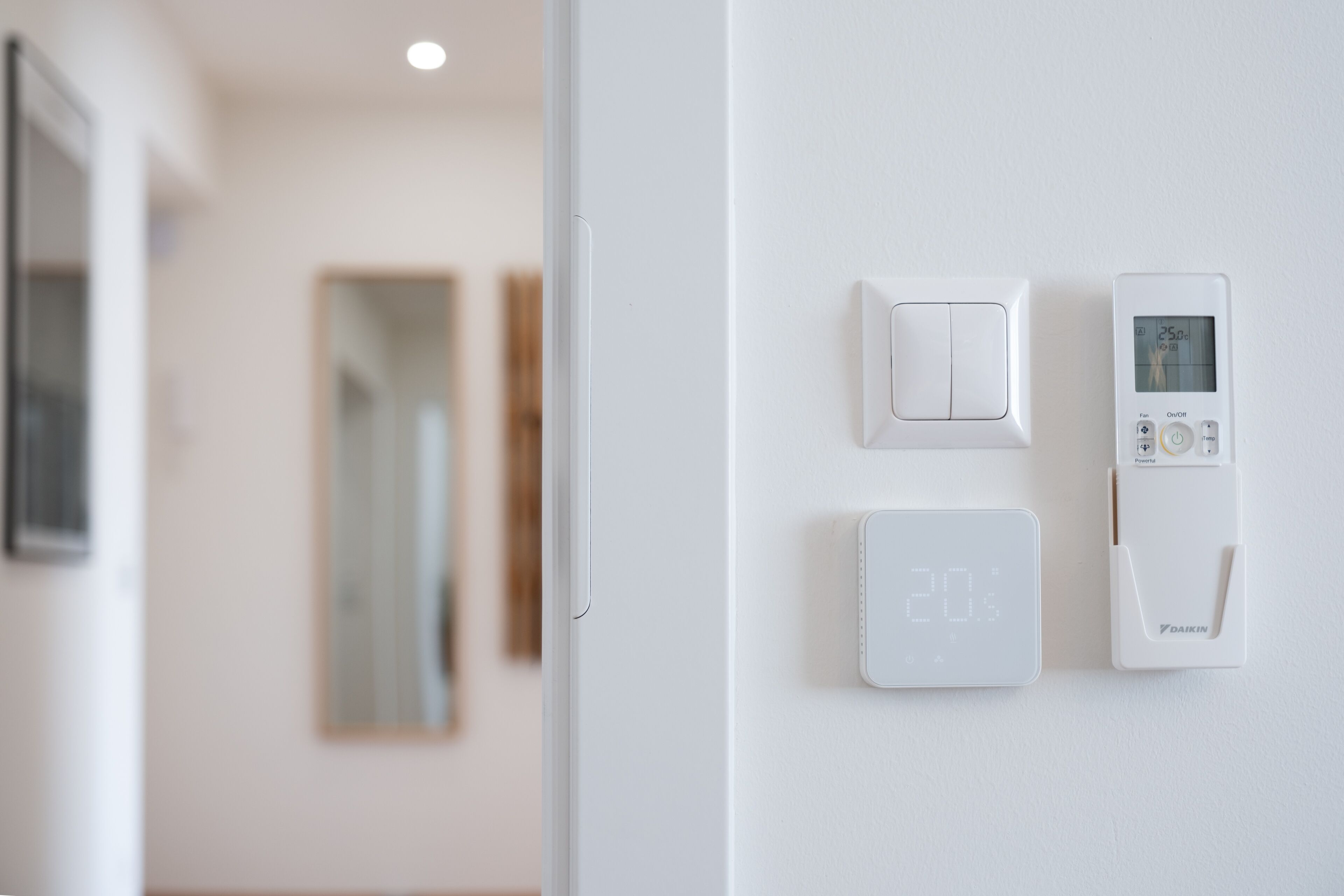 A thermostat and a light switch on a white wall.