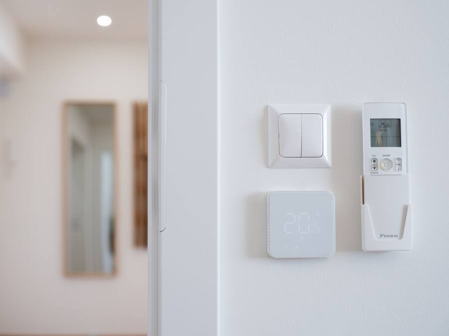 A thermostat and a light switch on a white wall.