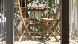 An outdoor wooden table and chairs set against a white metal fence, with a view of trees and a building in the background.