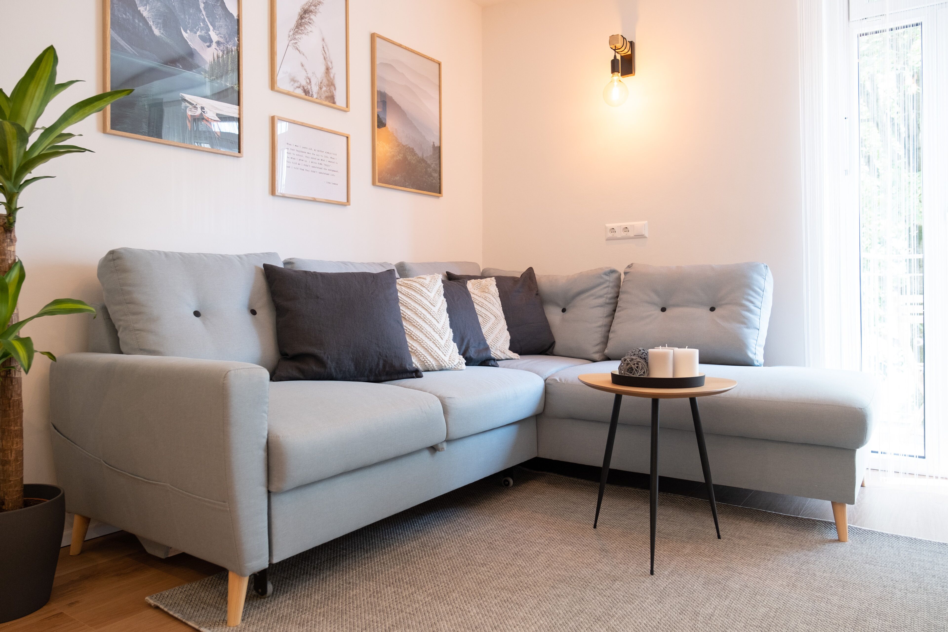 A modern living room with a light grey sectional sofa, a small round table with candles, and a potted plant.