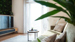 A modern living room with a sofa, a small side table, a television, and a green plant.