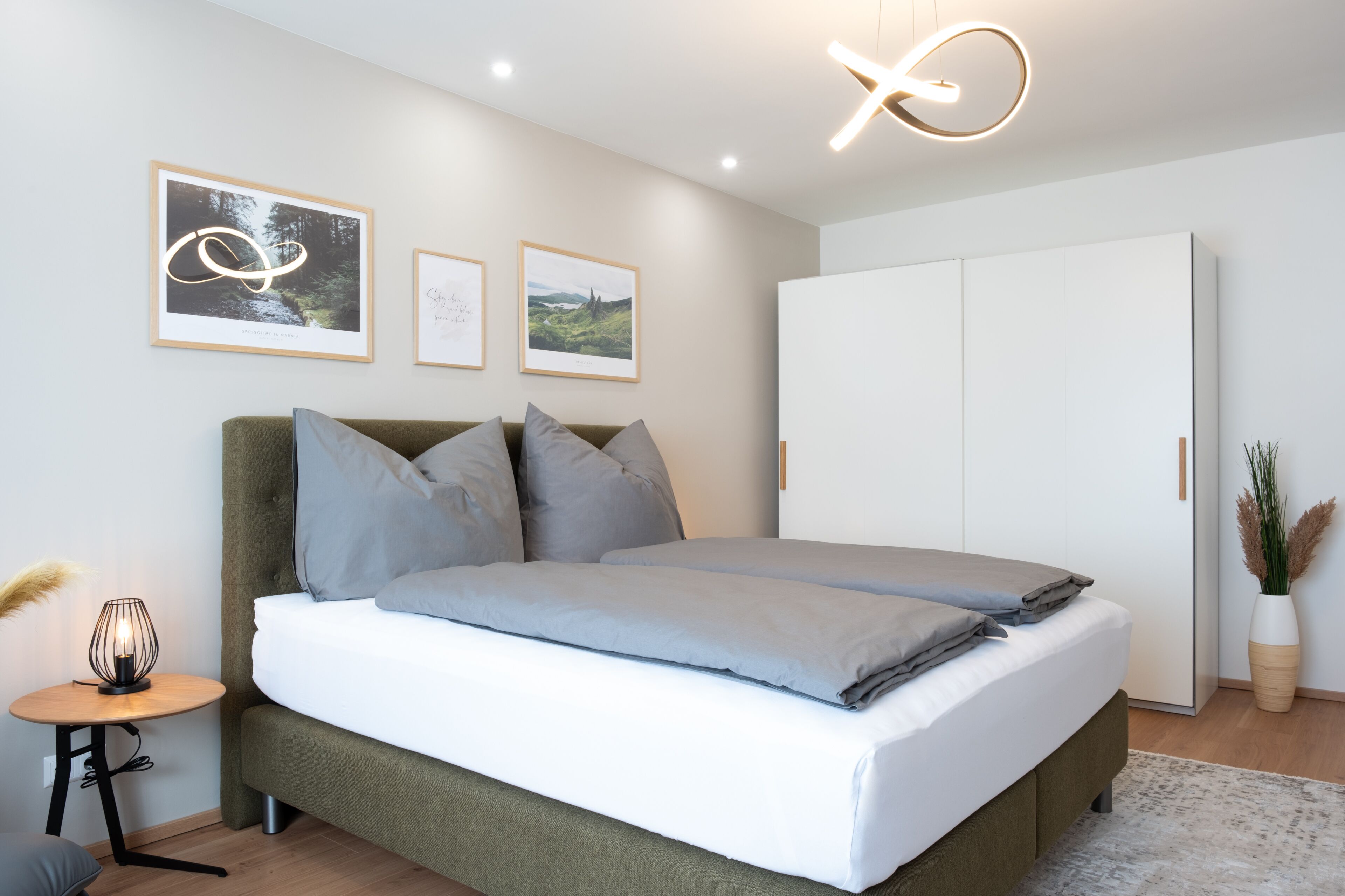 A modern bedroom with a large bed, a wardrobe, and framed pictures on the wall.