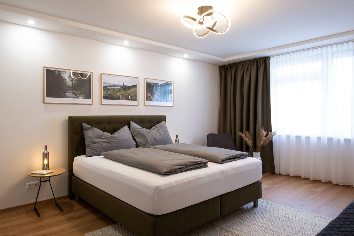 Un dormitorio moderno con una cama grande, una mesita de noche con lámpara y tres cuadros enmarcados en la pared.