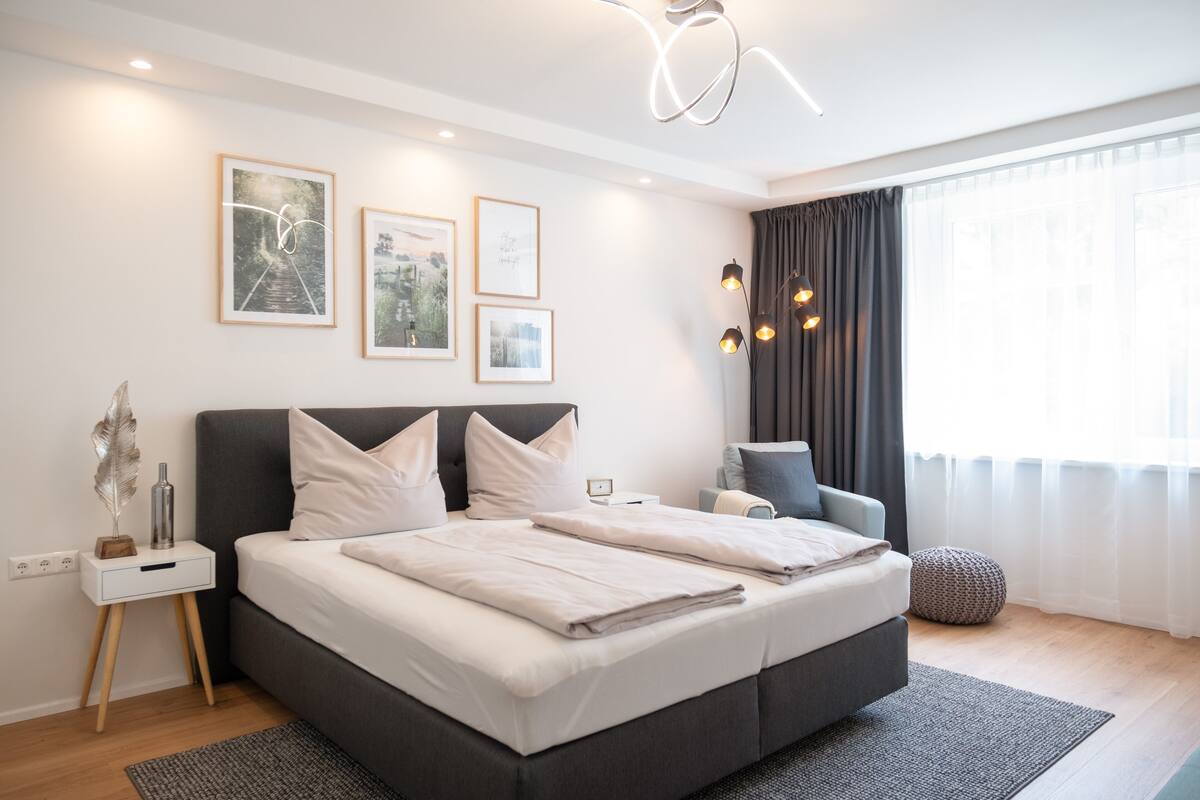 Un dormitorio moderno con una cama grande, mesitas de noche, un escritorio y una silla.