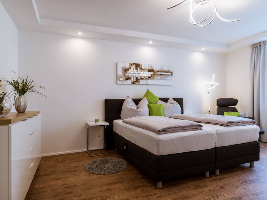 Un dormitorio moderno con una cama grande, una mesita de noche, una pequeña mesita auxiliar y una lámpara de pie.