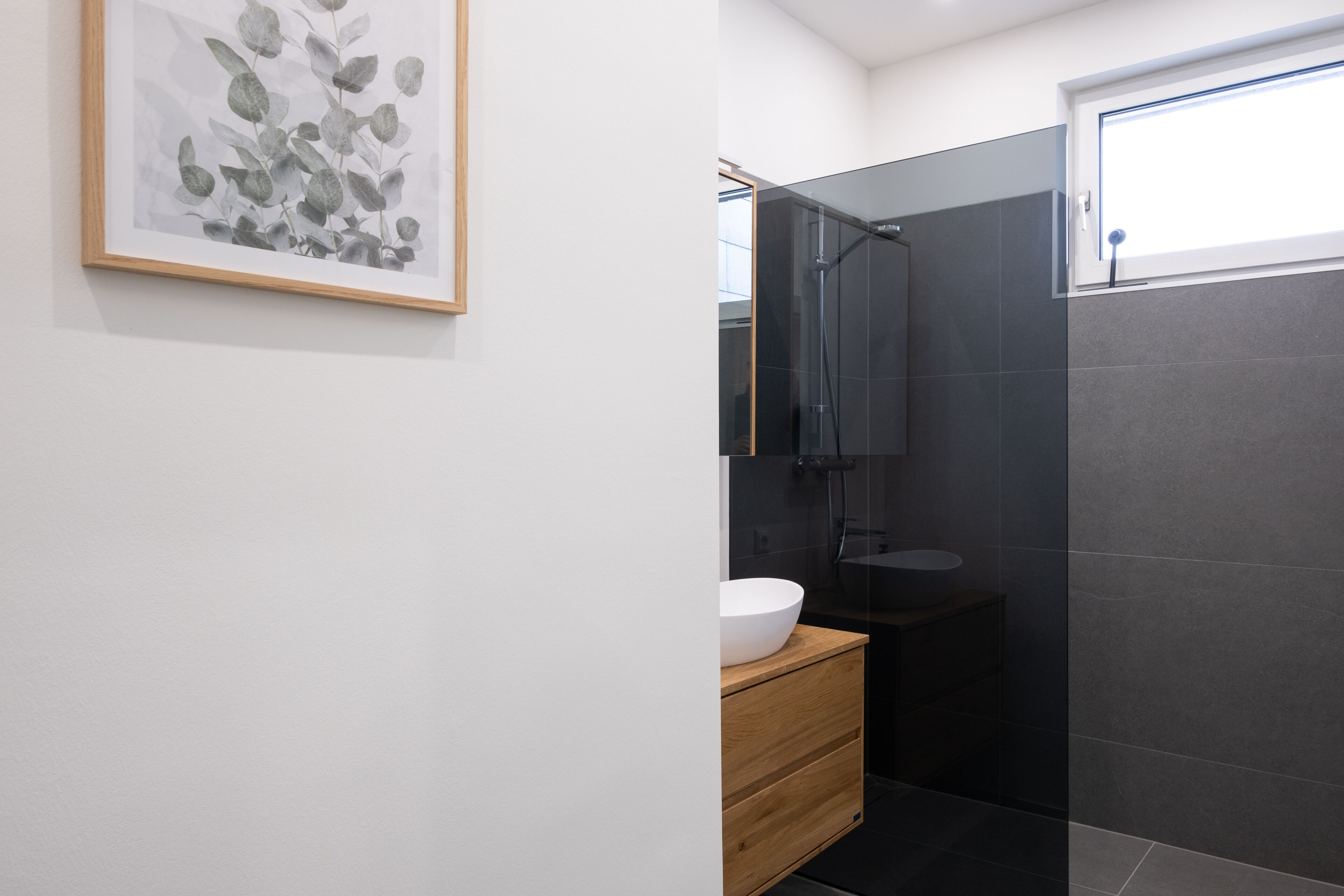 A modern bathroom with a glass shower enclosure, a white sink, and a wooden cabinet.