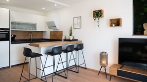 A modern kitchen with a central island, bar stools, a TV, and a small plant.