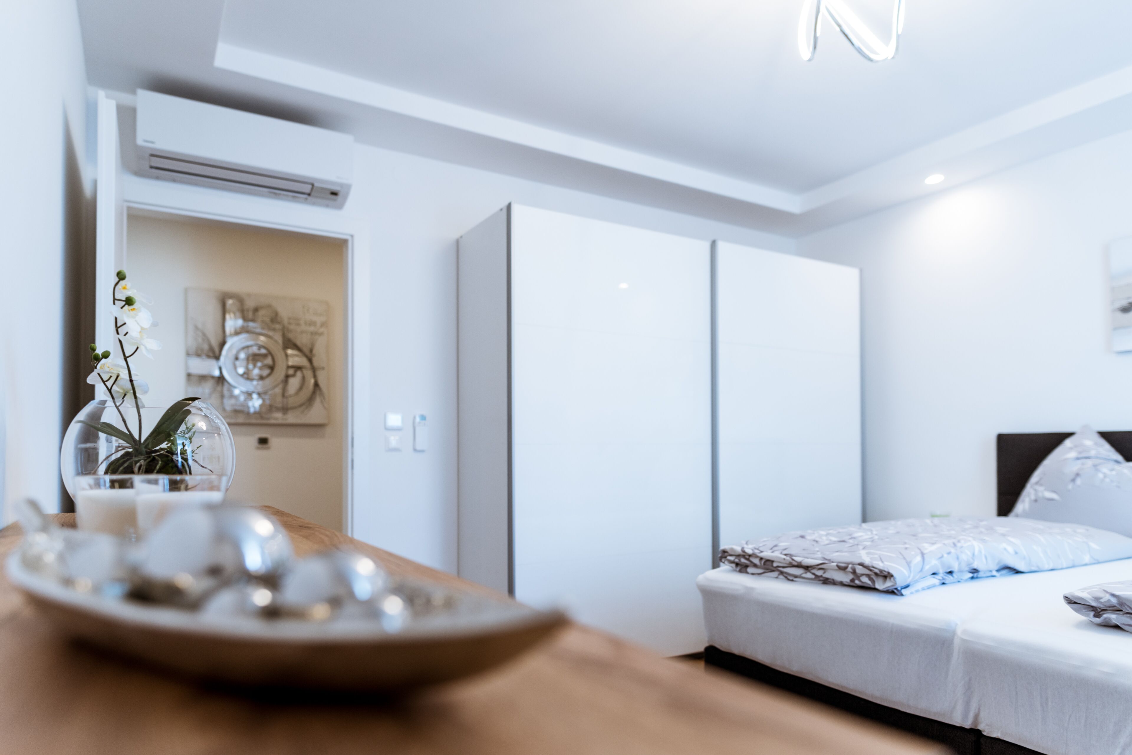 Een moderne hotelkamer met een bed, een nachtkastje met een fruitschaal, een potplant en een wandairconditioner.