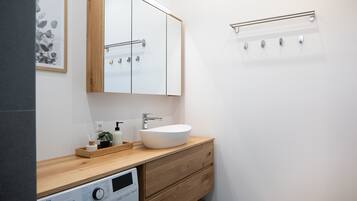 Een moderne badkamer met een houten wastafel, een witte wasbak, een spiegel en een wasmachine.