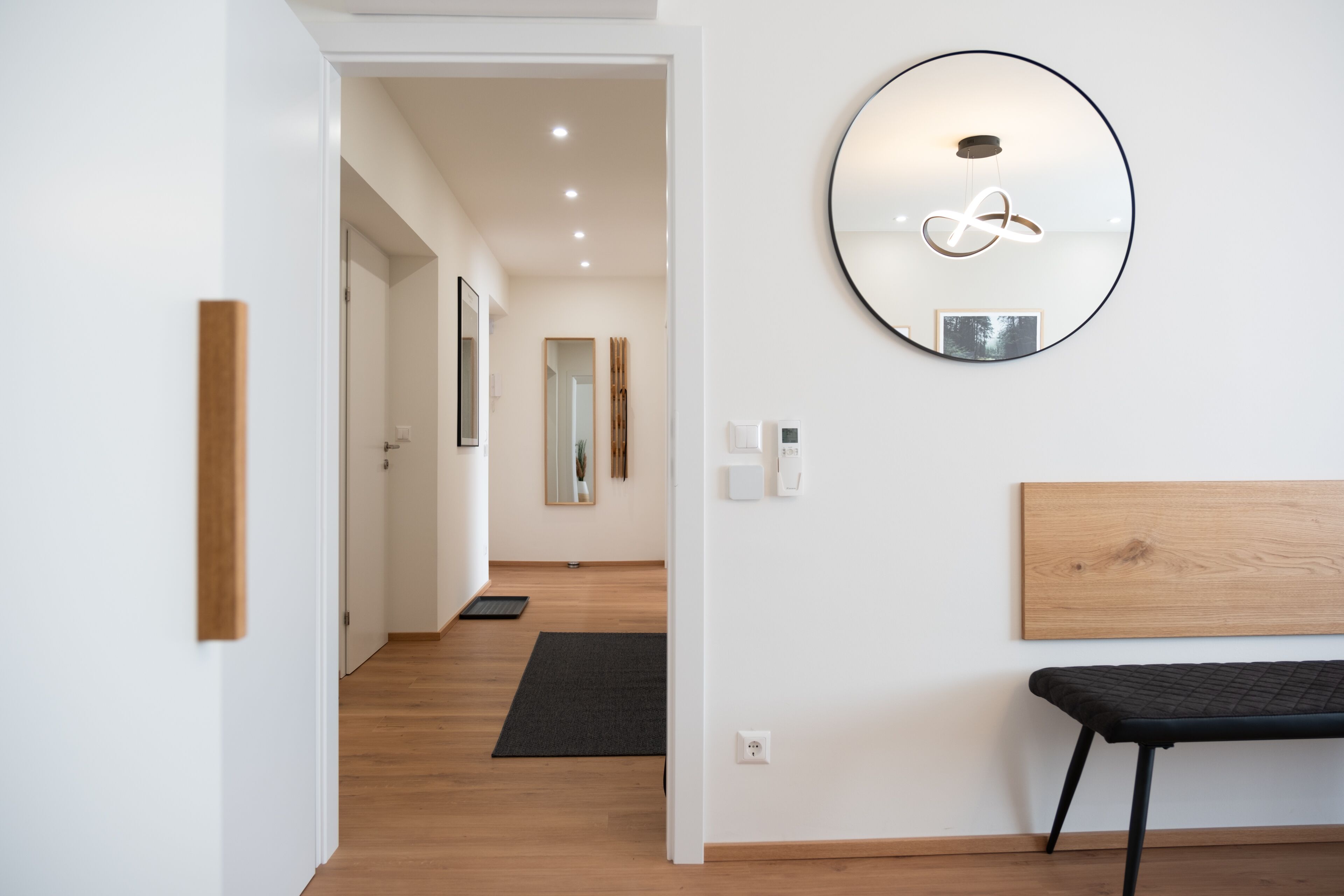 A modern hallway with a wooden bench, a round mirror, and a wooden headboard.