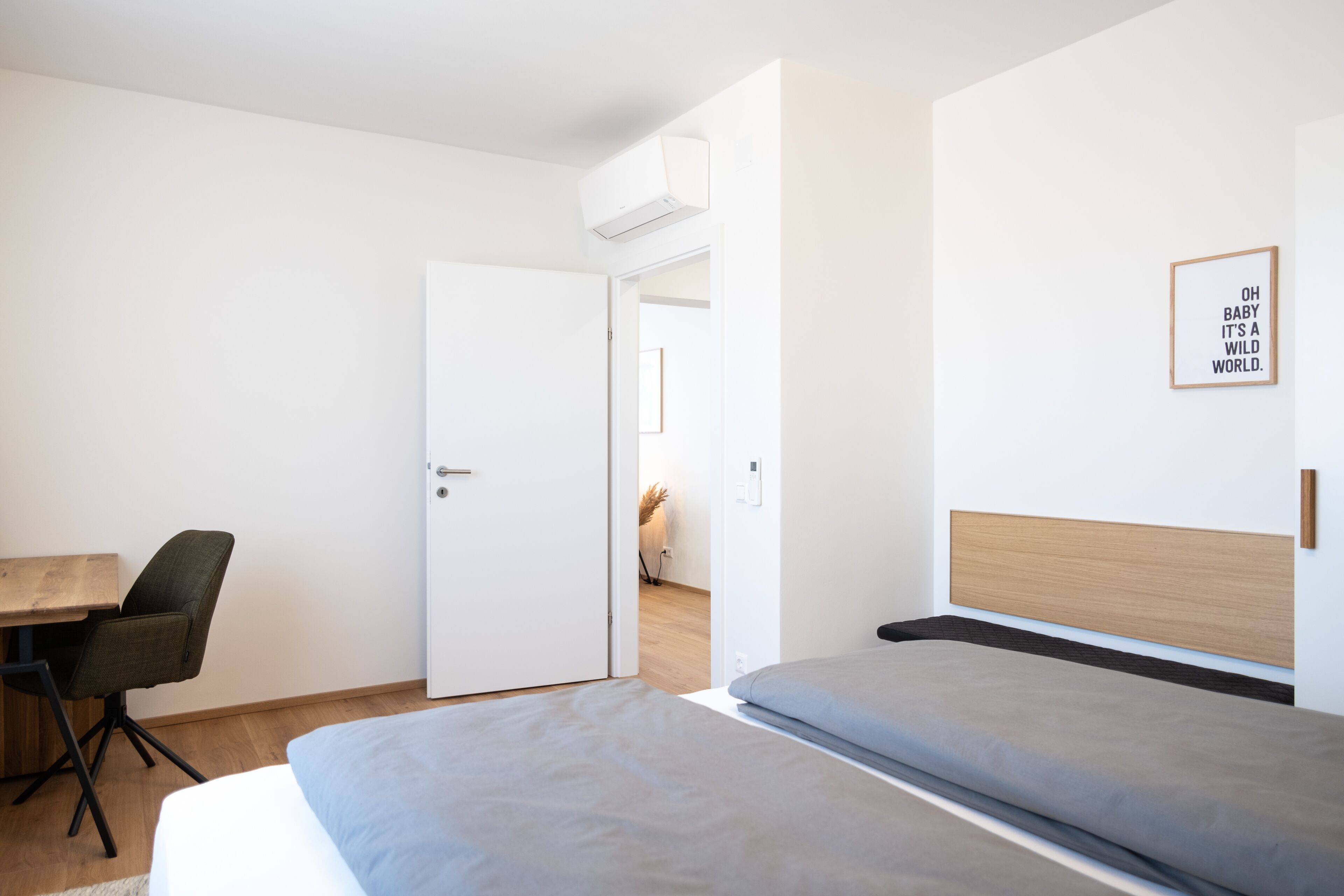 Un dormitorio moderno con cama, escritorio y silla. Hay una puerta que conduce a otra habitación.