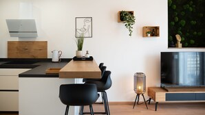 Una cocina moderna con una isla de madera, sillas negras, un hervidor blanco y una obra de arte enmarcada en la pared.