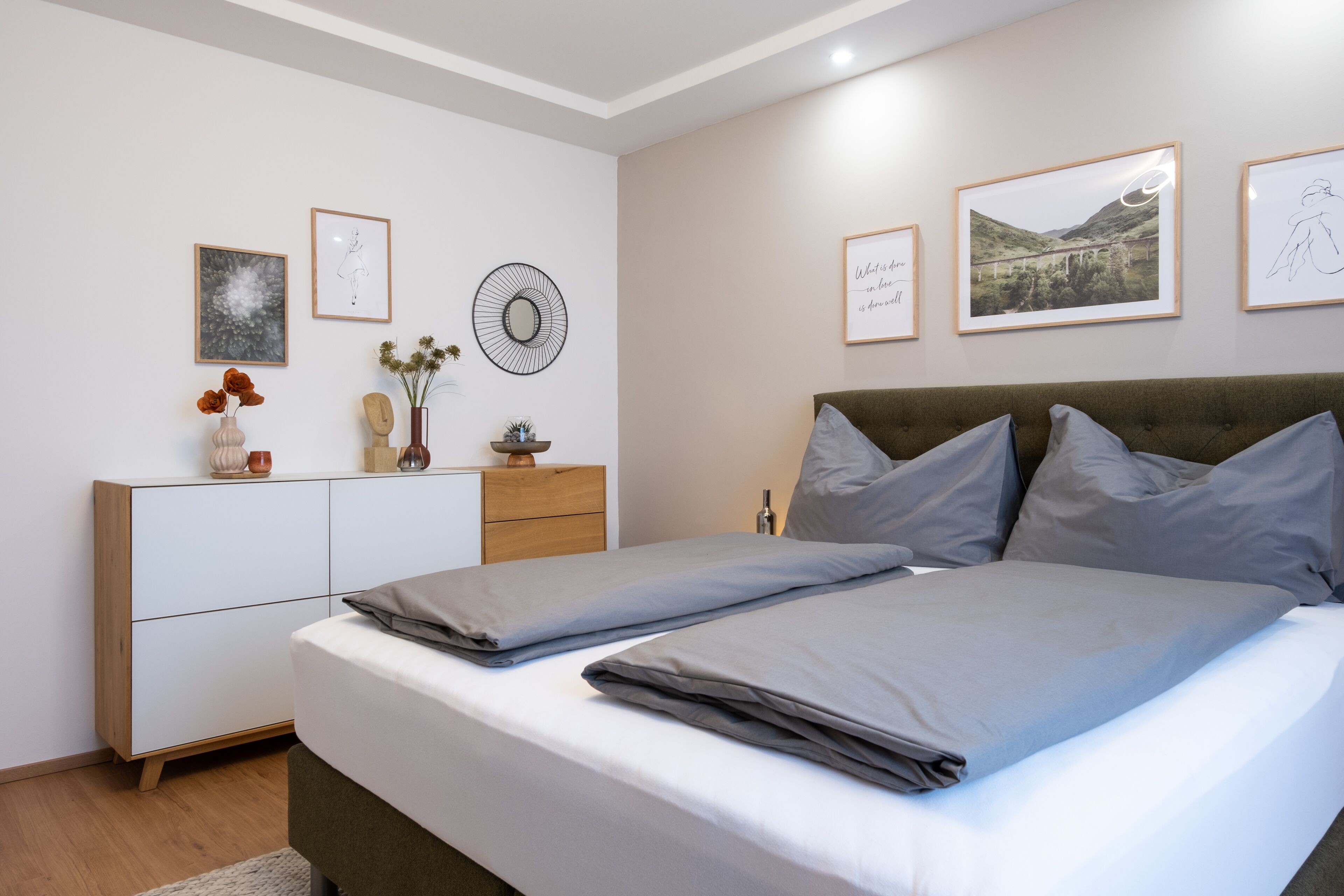 Ein ordentlich eingerichtetes Schlafzimmer mit Bett, Kommode und Wandbildern.
