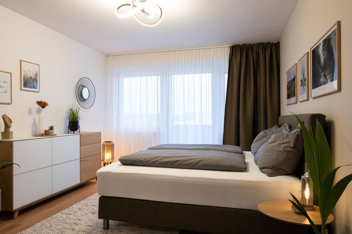 Un dormitorio moderno con cama, mesita de noche y un ventanal con cortinas.