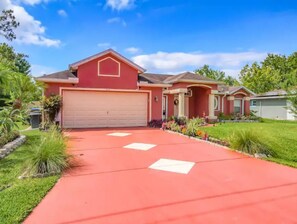Stunning single-story home surrounded by lush greenery and a beautifully paved driveway.